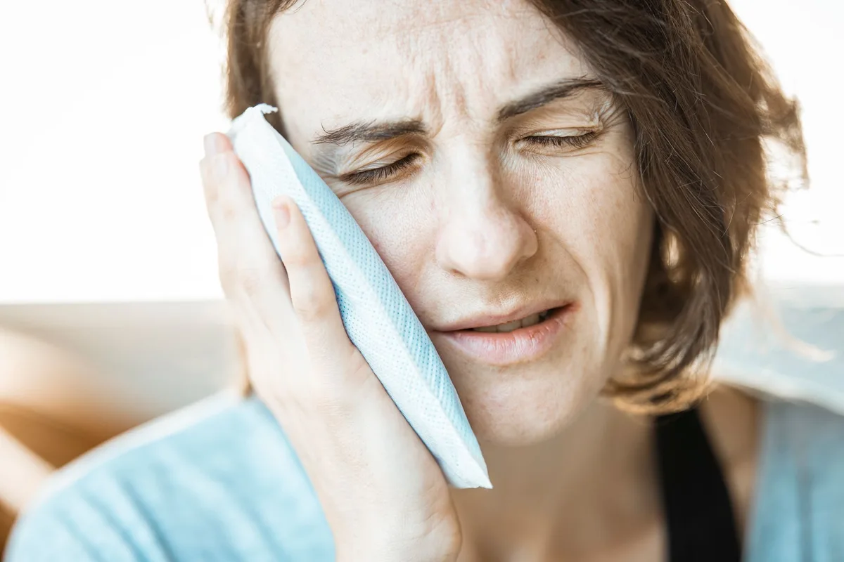 Person applying a cold compress to the forehead to relieve migraine pain