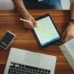 Hands holding tablet showing abstract casino icons next to paperwork on a desk