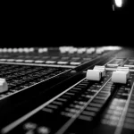 Hands over an audio mixing console with a waveform display in a bright studio