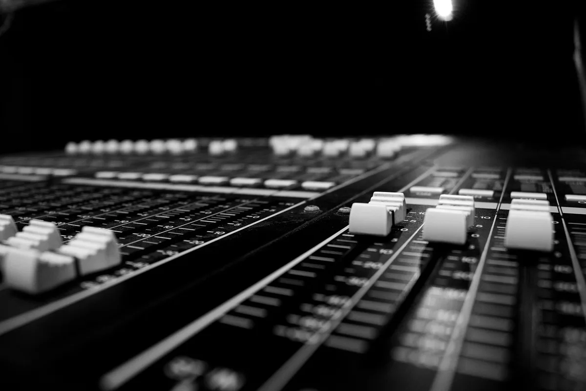 Hands over an audio mixing console with a waveform display in a bright studio