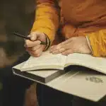 Notebook open showing the number 131 with hands pointing and books in the background