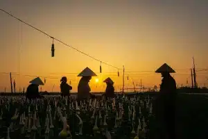 Three silhouetted figures walking past a small wooden church near a riverbank at dusk