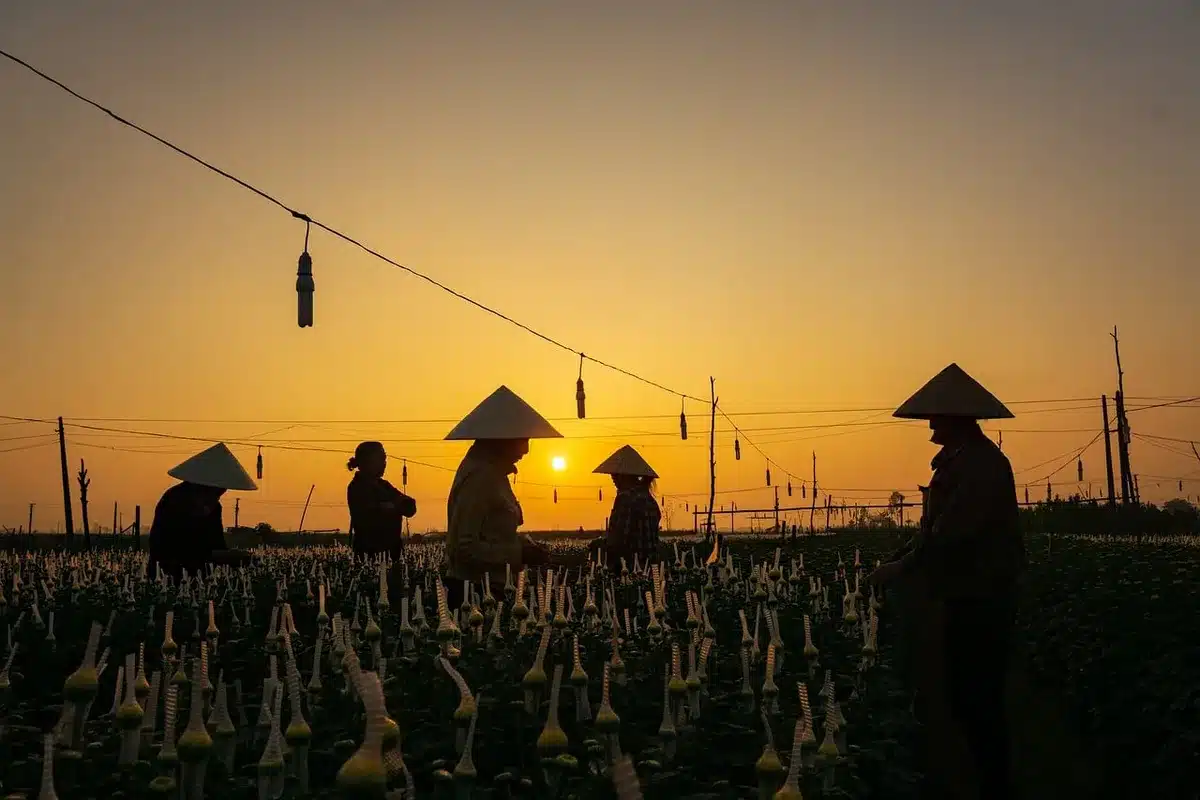 Three silhouetted figures walking past a small wooden church near a riverbank at dusk