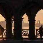 Silhouette of a damaged city bridge over a river with empty lanes and a pedestrian on the bank