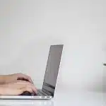 Open office desk with laptop, mug and reports, anonymous worker in background