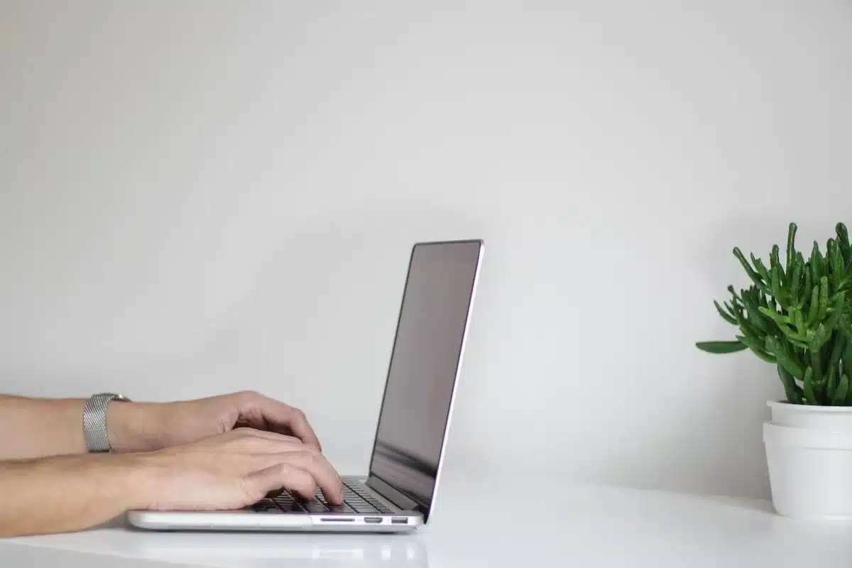 Open office desk with laptop, mug and reports, anonymous worker in background